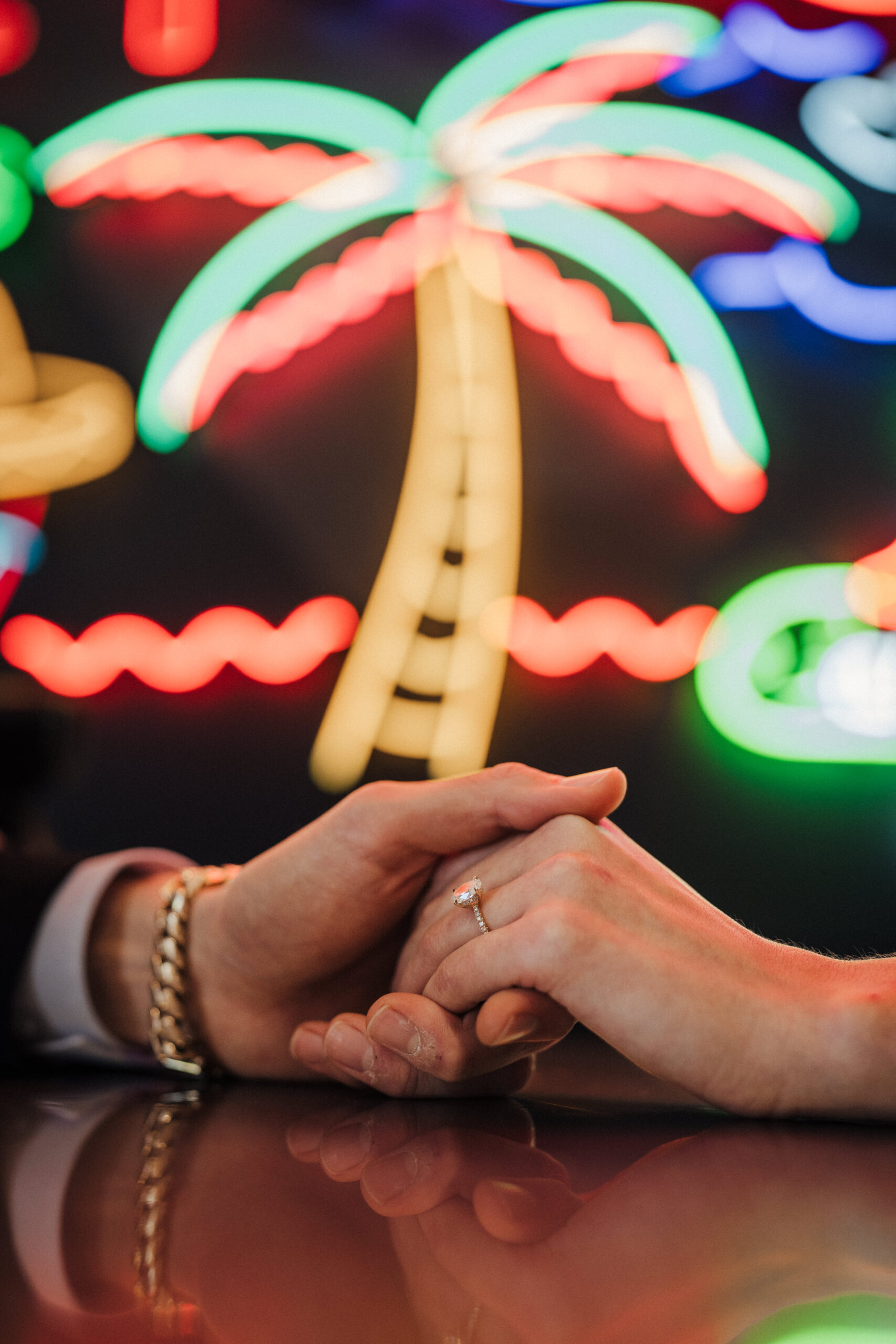 A couple holds hands in front of the neon signs in the Grand Central Market in Downtown Los Angeles.  Engagement ring shot.