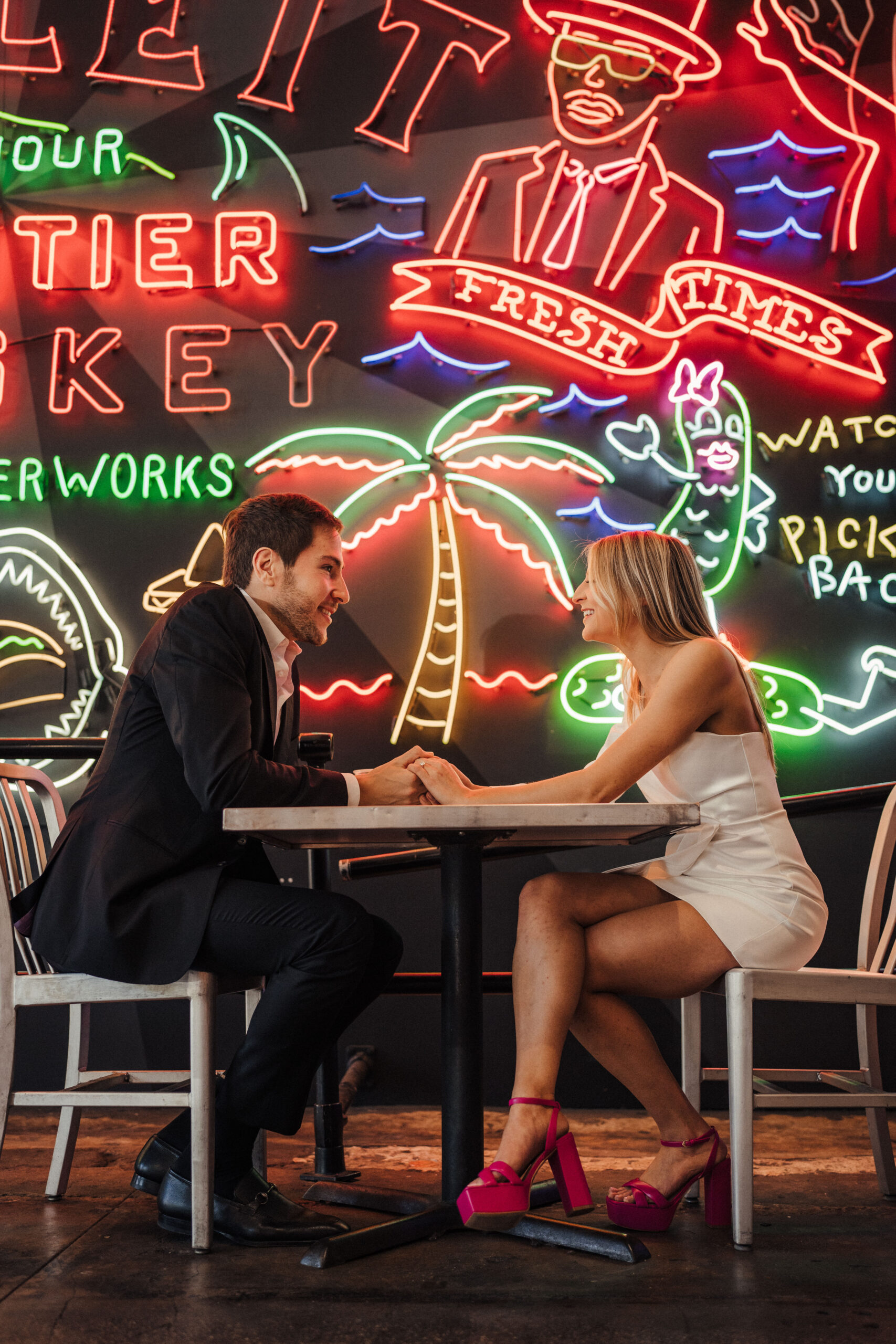 A couple takes their engagement photos in Grand Central Market in Downtown Los Angeles in front of the neon signs.