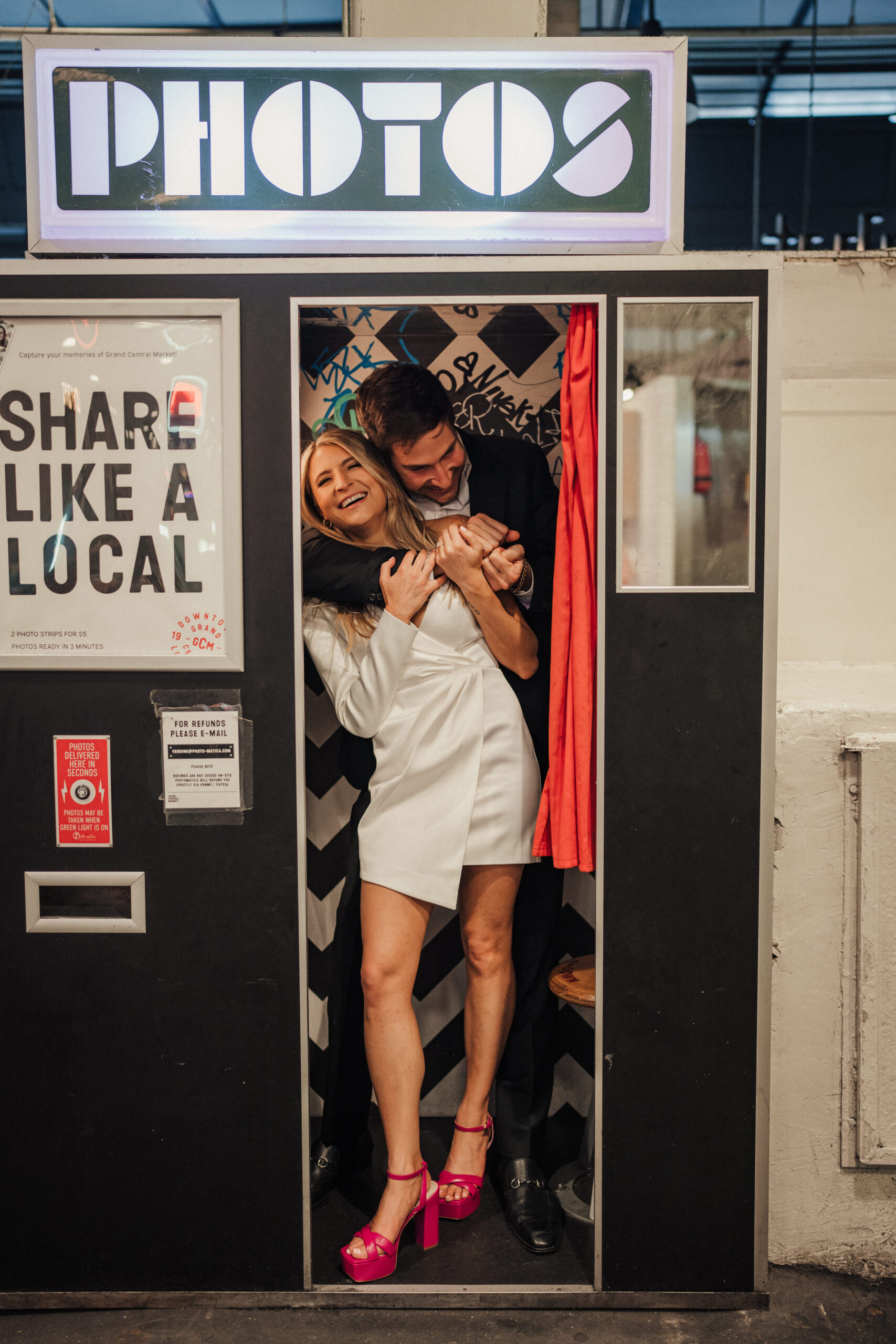 Engaged couple takes photos together in a photo booth at Grand Central Market in Downtown LA for engagement session