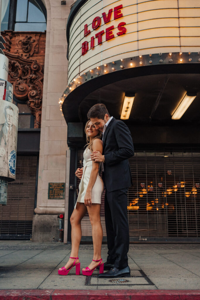 Engaged couple takes urban engagement photos in front of a theater sign at Grand Central Market in Downtown LA