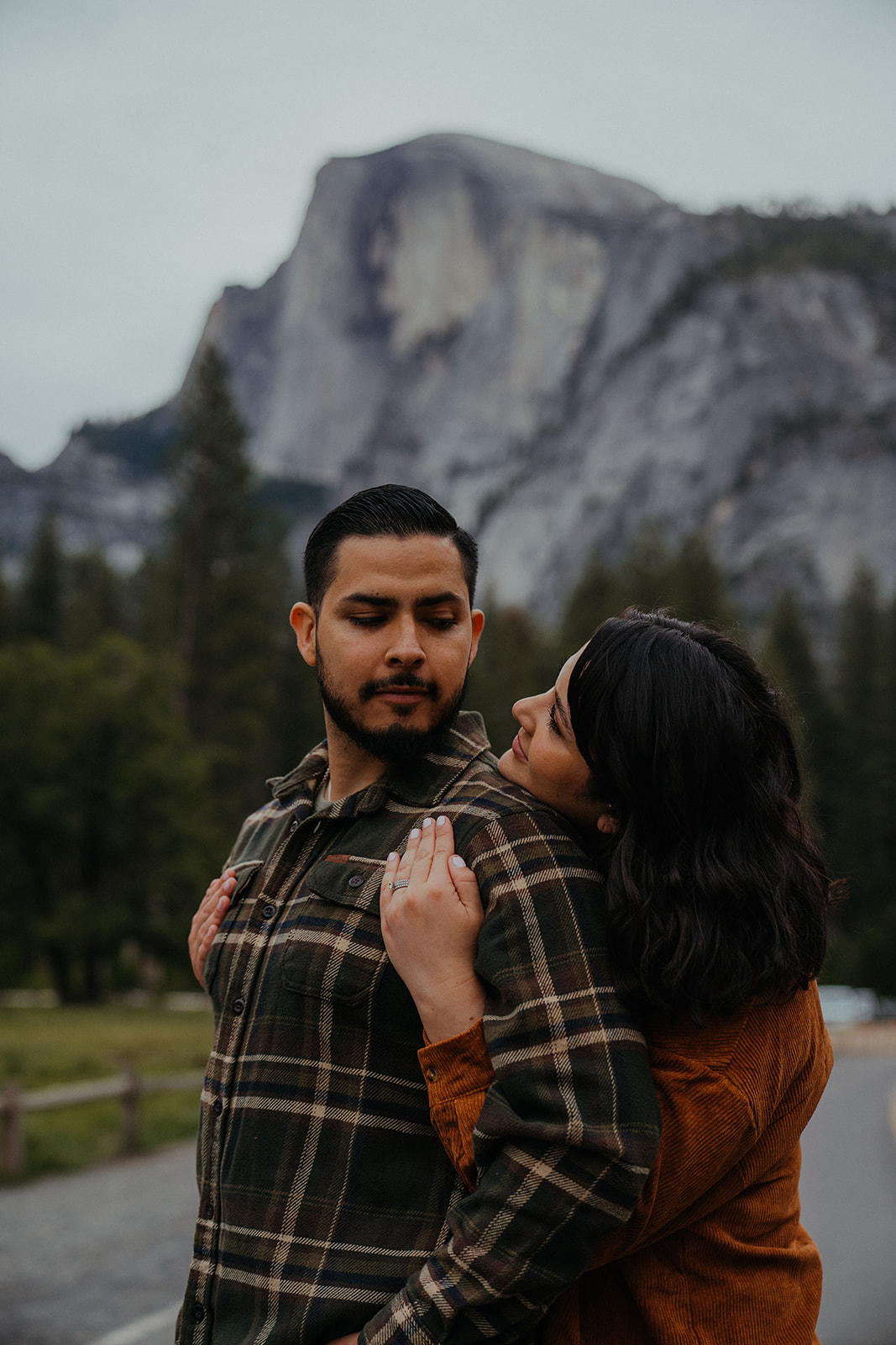 Adventurous Couple walks through the Yosemite Valley floor, holding hands and embracing each other under Upper Yosemite Falls. 